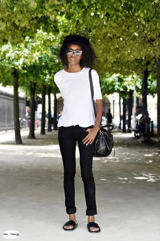 Jongedame draagt wit T-shirt, zwarte broek, zwarte sandalen en een zwarte handtas