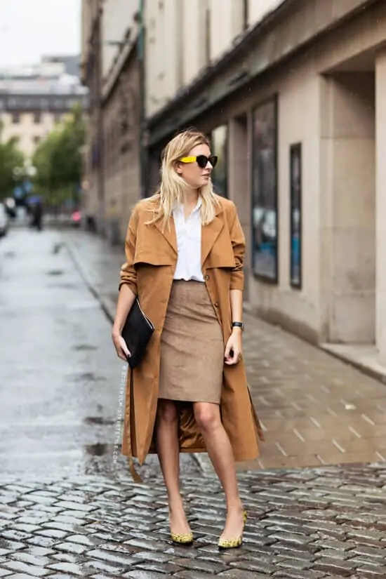 Stijlvolle dame draagt een lange camel regenjas, een witte blouse, een beige kokerrok, een zwarte clutch en flashy pumps - 10 leuke street style blogs voor modeliefhebbers