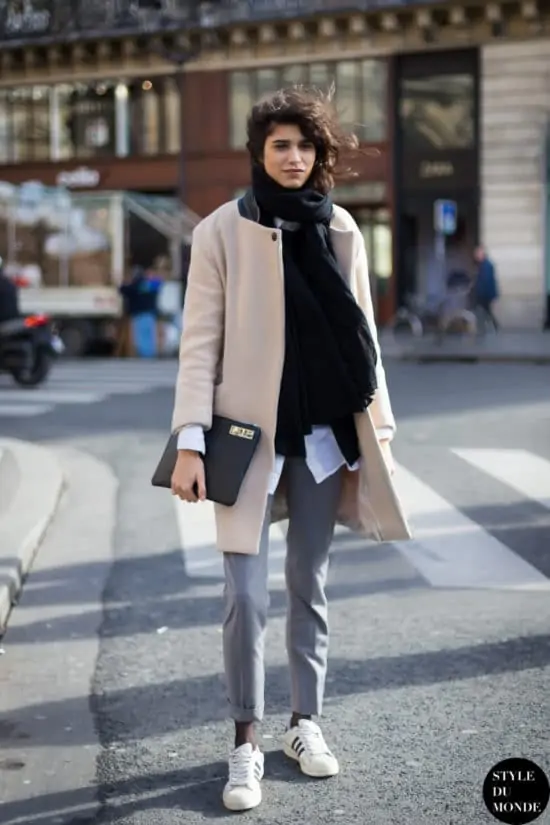 Stijlvolle dame draagt een lange beige overjas, een grijze broek, een zwarte sjaal, witte sneakers en een zwarte clutch - 10 leuke street style blogs voor modeliefhebbers